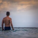 topless man in blue shorts standing on water during daytime